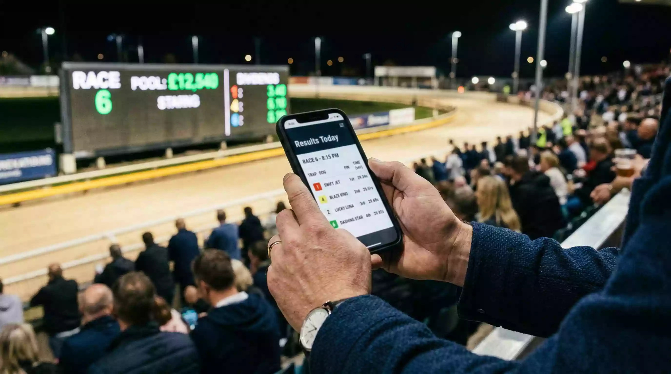 Person checking greyhound race results on a smartphone at a stadium